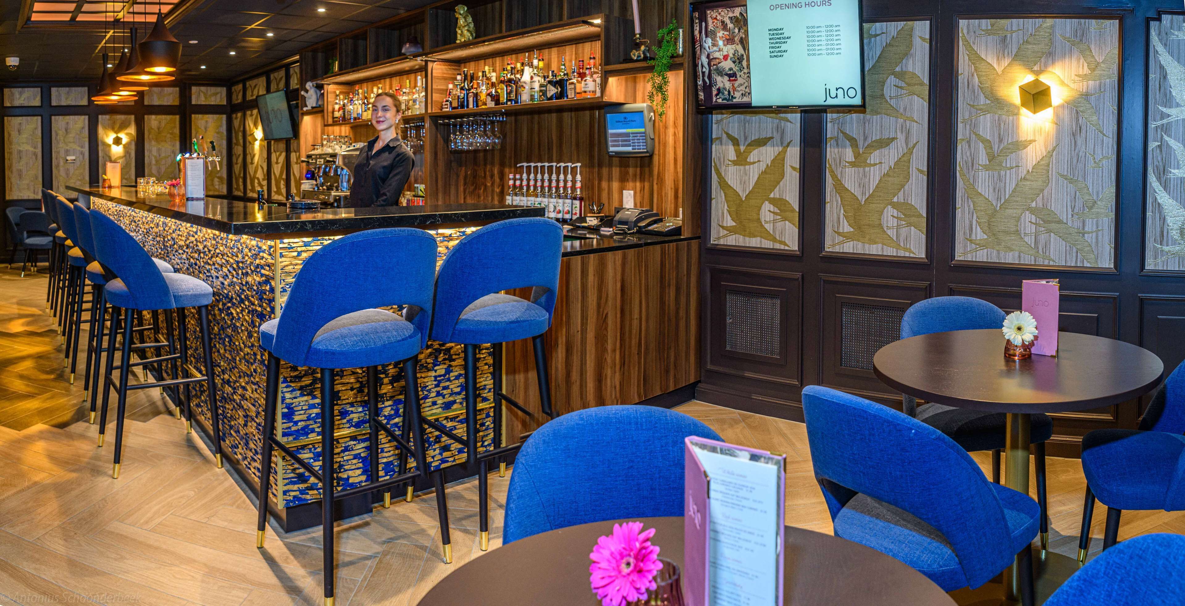 A bar area with a bartender, blue bar stools, and a menu board.