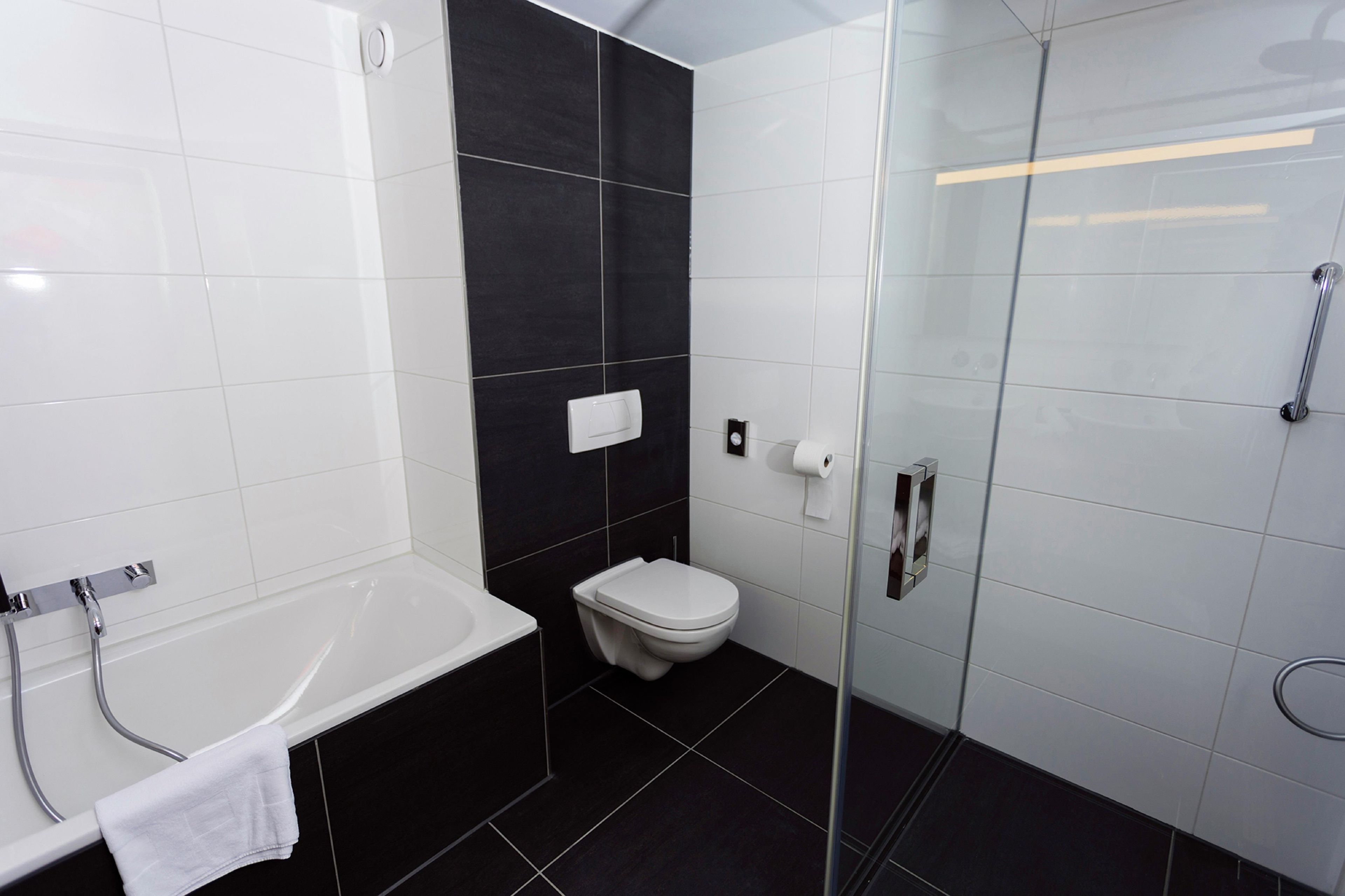 A modern bathroom with a white bathtub, a white toilet, and a glass-enclosed shower area.
