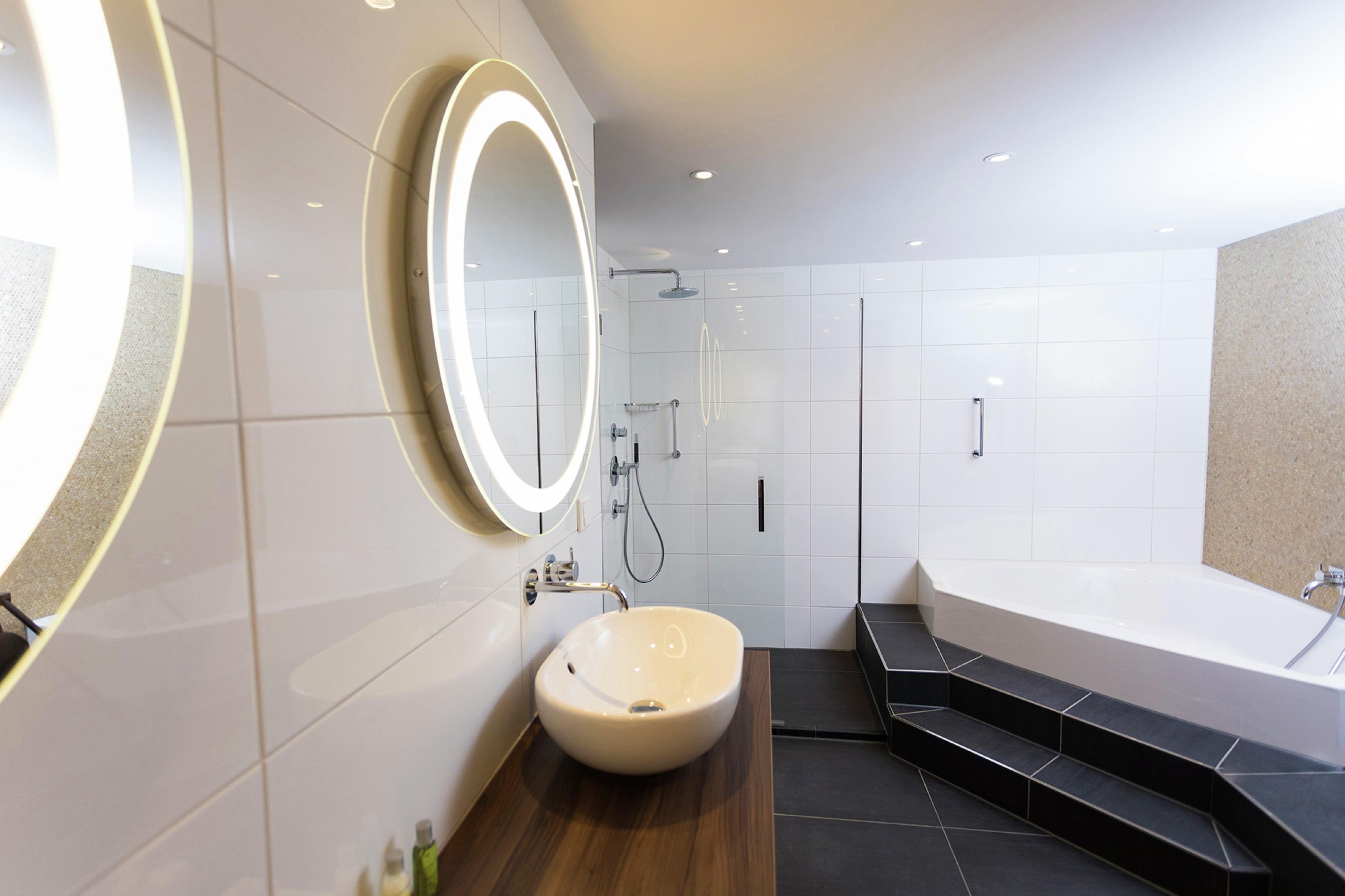 A modern bathroom with a large freestanding bathtub, a round sink, and a walk-in shower.