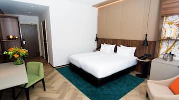 Quarto de hotel com cama, mesa de cabeceira, abajur, cadeira, escrivaninha e um vaso com flores.