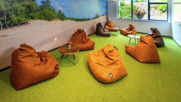 A room with green carpet, bean bags, a small table with a vase, and a mural of a landscape.