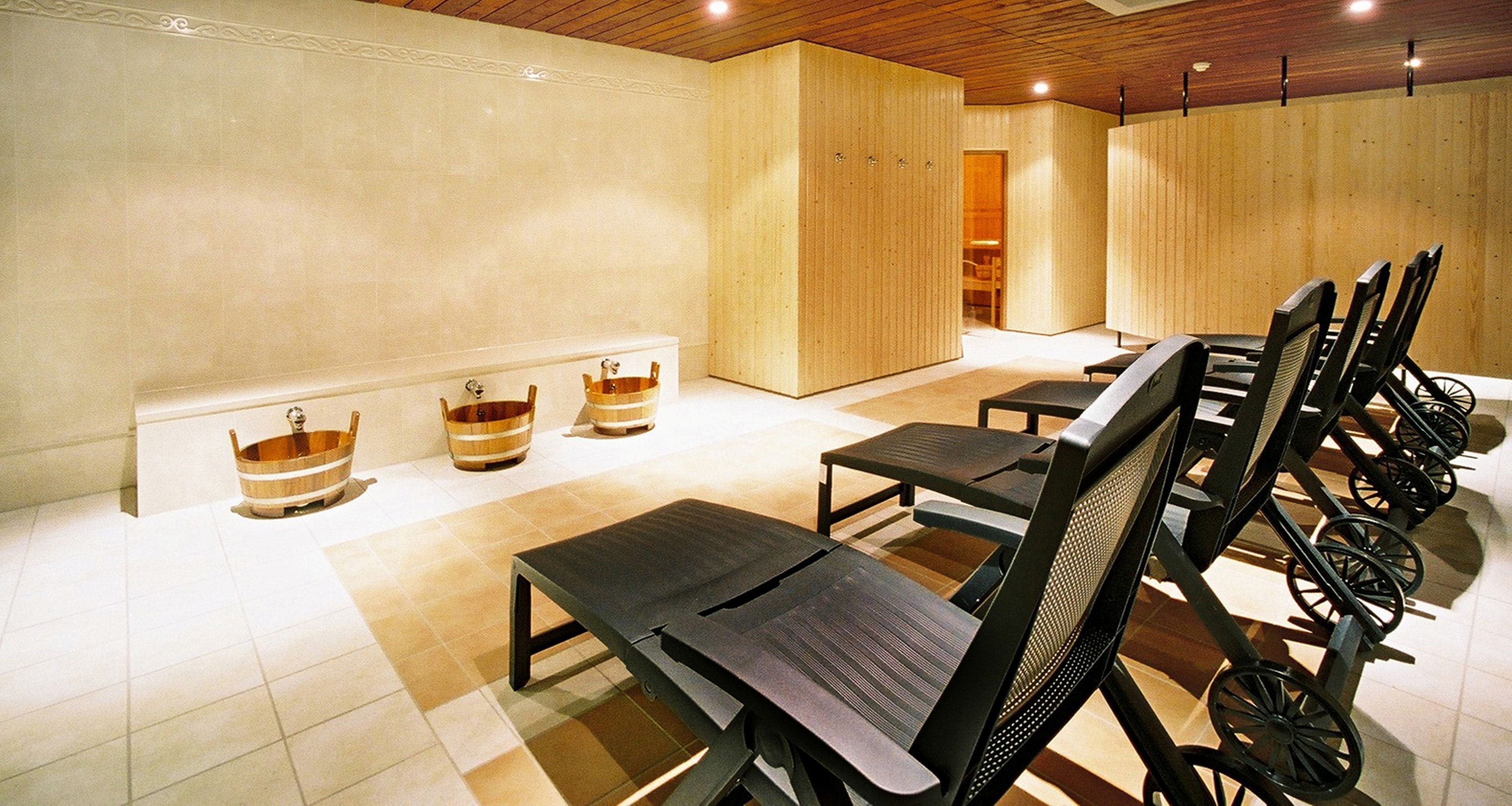 Un cuarto de spa con tinas de madera, sillas negras y piso de baldosas.