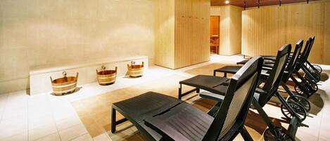 A spa room with wooden tubs, black chairs, and a tiled floor.