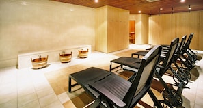 A spa room with wooden tubs, black chairs, and a tiled floor.