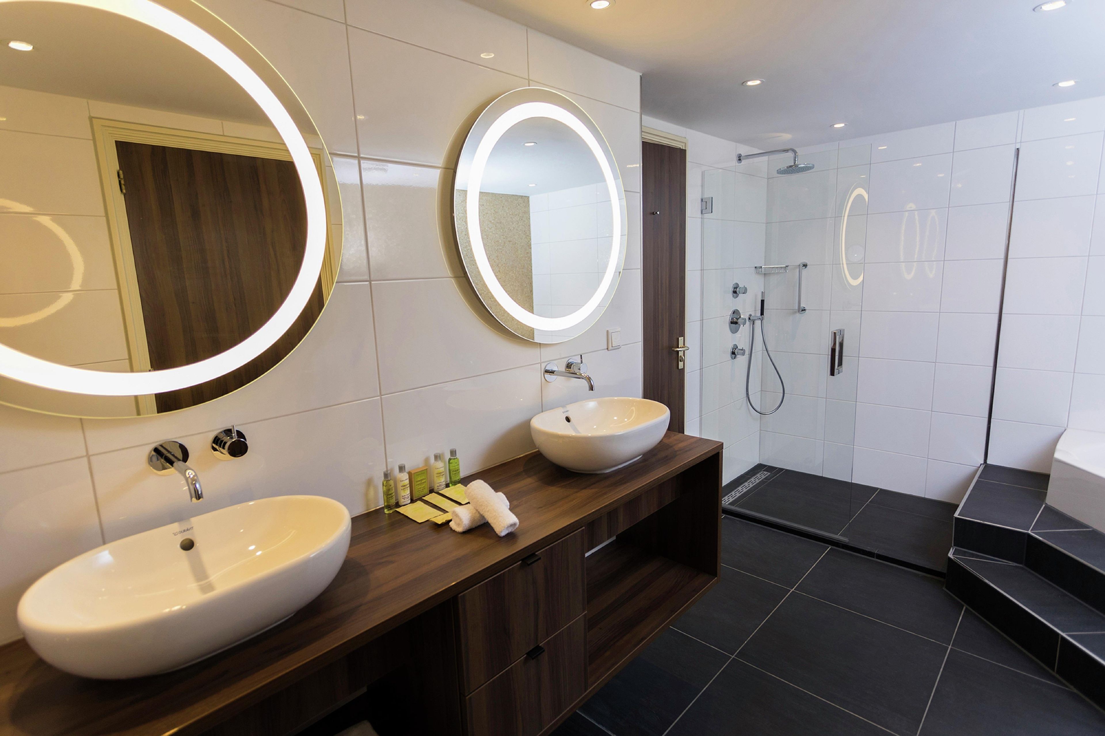 Un baño moderno con dos lavamanos, un espejo grande y una zona de ducha.