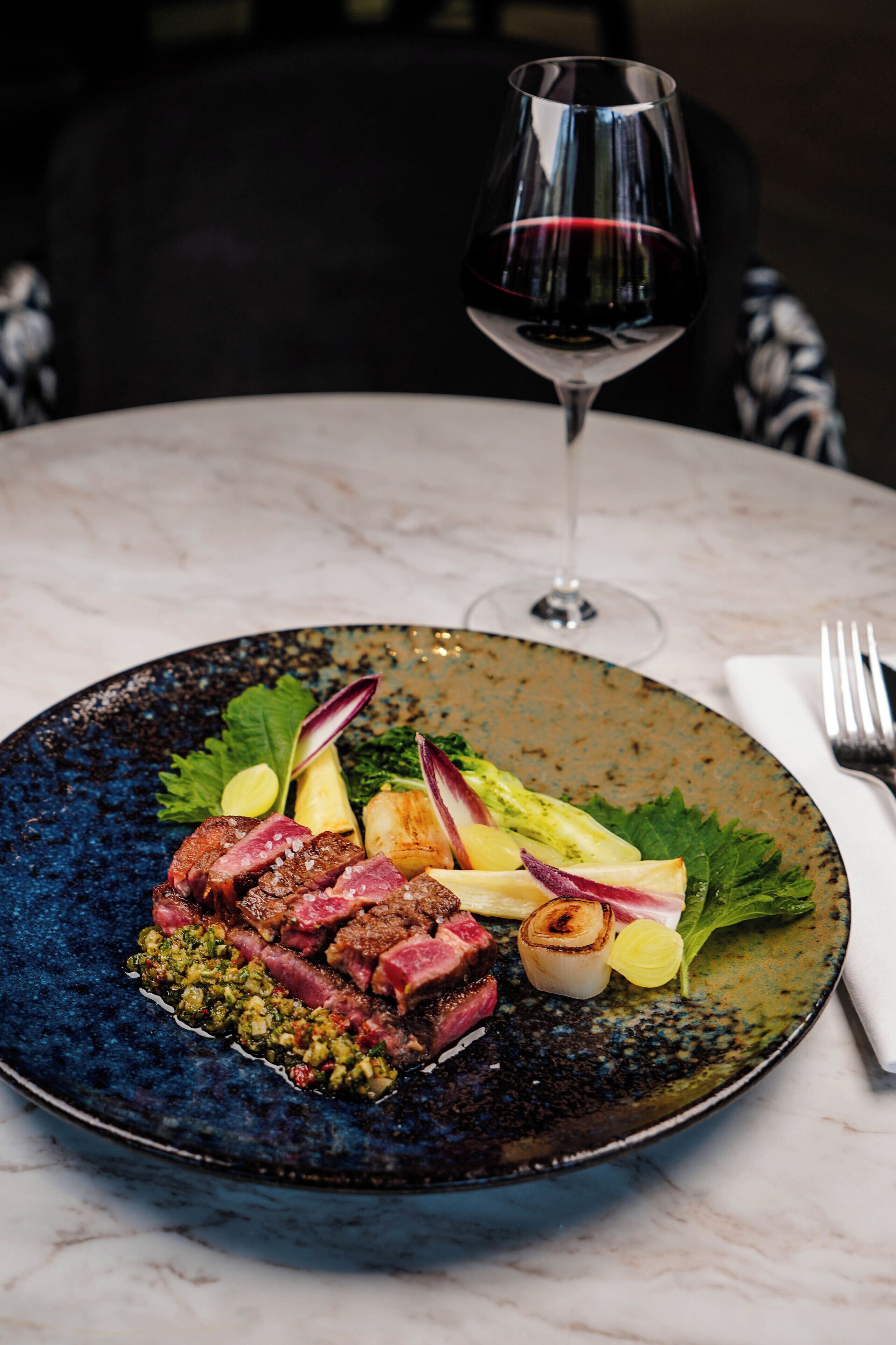 Un plato de comida con una copa de vino tinto sobre una mesa.
