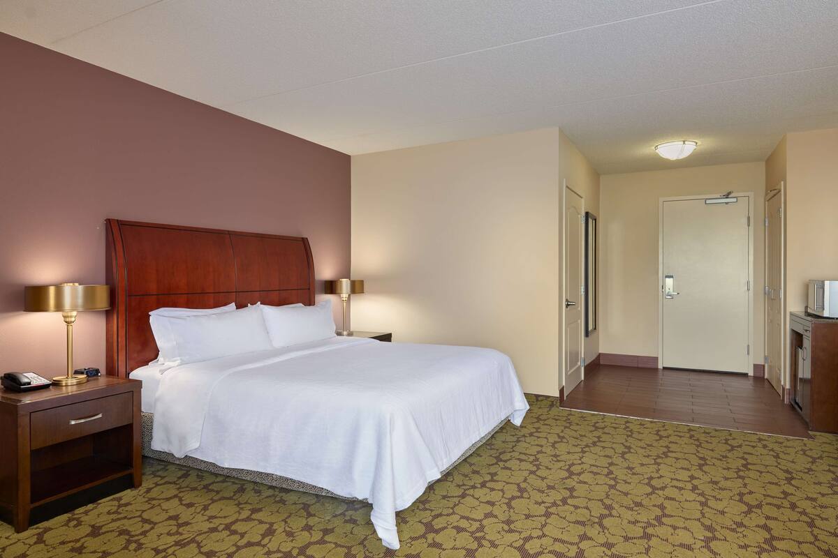 A hotel room with a wooden headboard, a white bedspread, a bedside lamp, a telephone, and a patterned carpet.