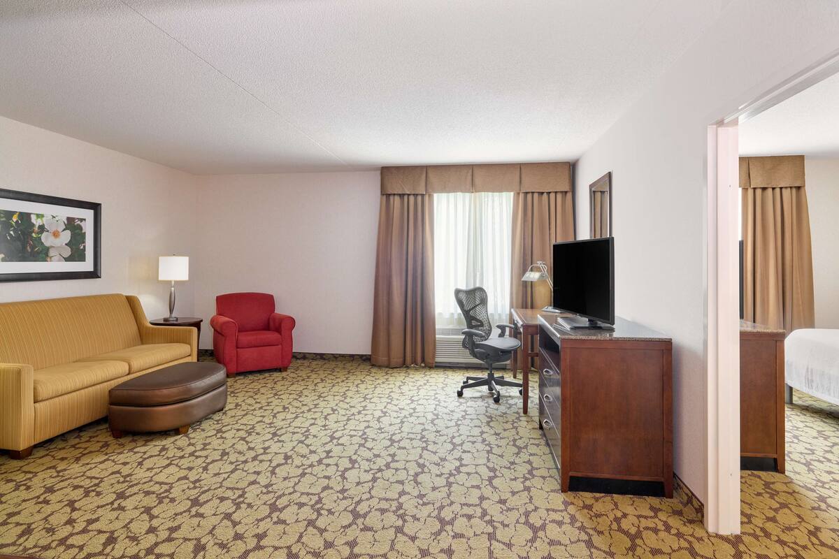 A hotel room with a yellow sofa, red armchair, and a desk with a television.