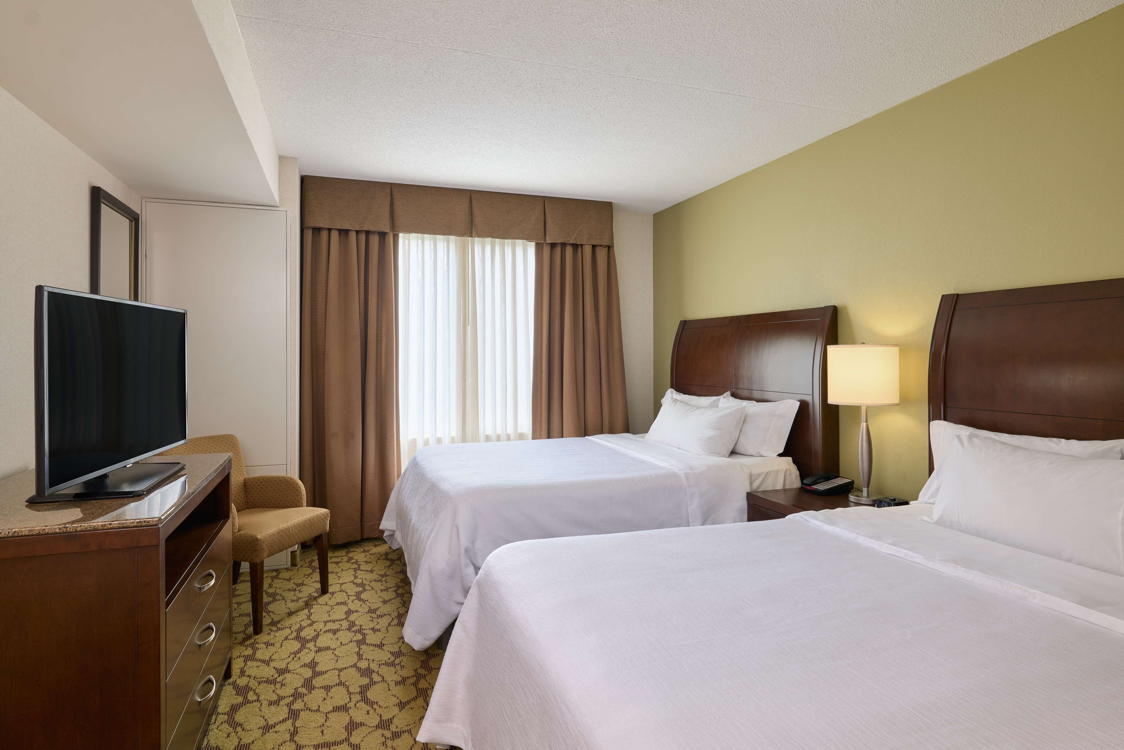 A hotel room with two beds, a TV, a desk, and a lamp.