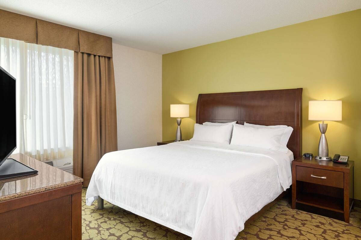 A hotel room with a large bed, two bedside tables with lamps, a desk with a TV, and a patterned carpet.