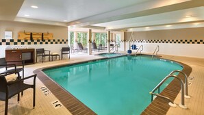 An indoor swimming pool with a checkered tile border, lounge chairs, and a poolside area with a view of trees.
