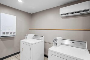A laundry room with two front-loading washing machines and an air conditioning unit mounted on the wall. - Microtel Inn by Wyndham Georgetown (Georgetown)