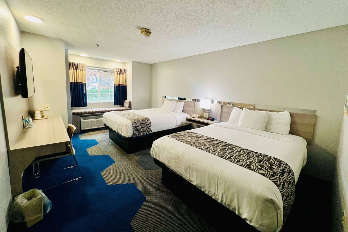 A hotel room with two beds, a desk, a chair, a TV, and a window with curtains.