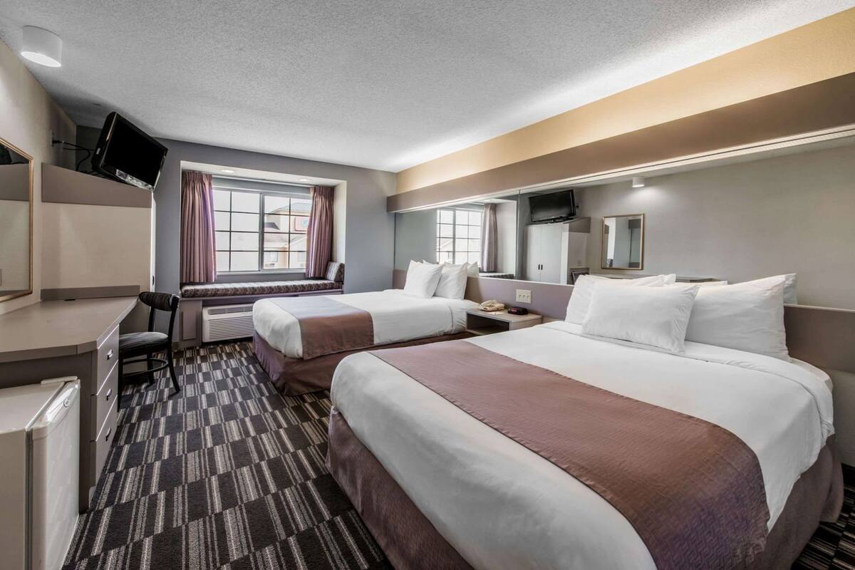 A hotel room with two beds, a desk, a TV, and a window with curtains.