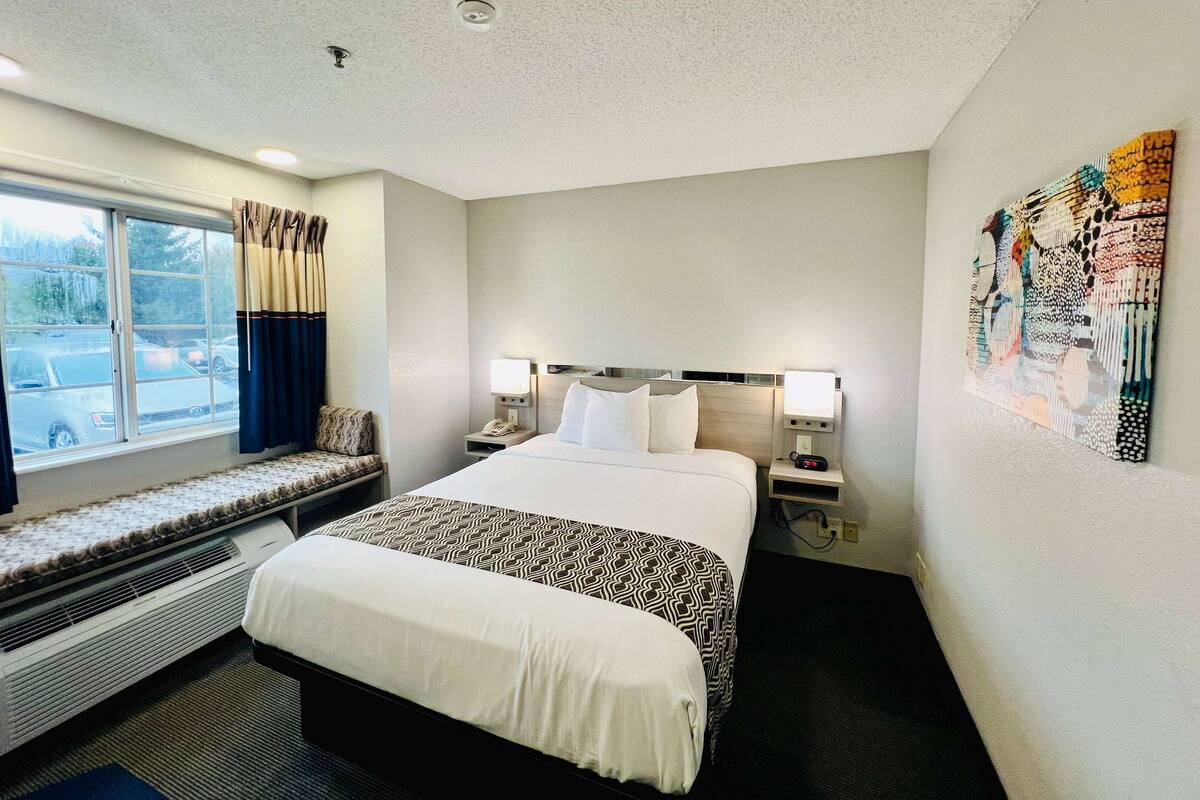 A hotel room with a large bed, a bench by the window, a heater, and a wall art piece.