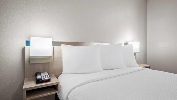 Una habitación de hotel con una cama bien hecha, una mesita de noche con un teléfono y una lámpara de pared.