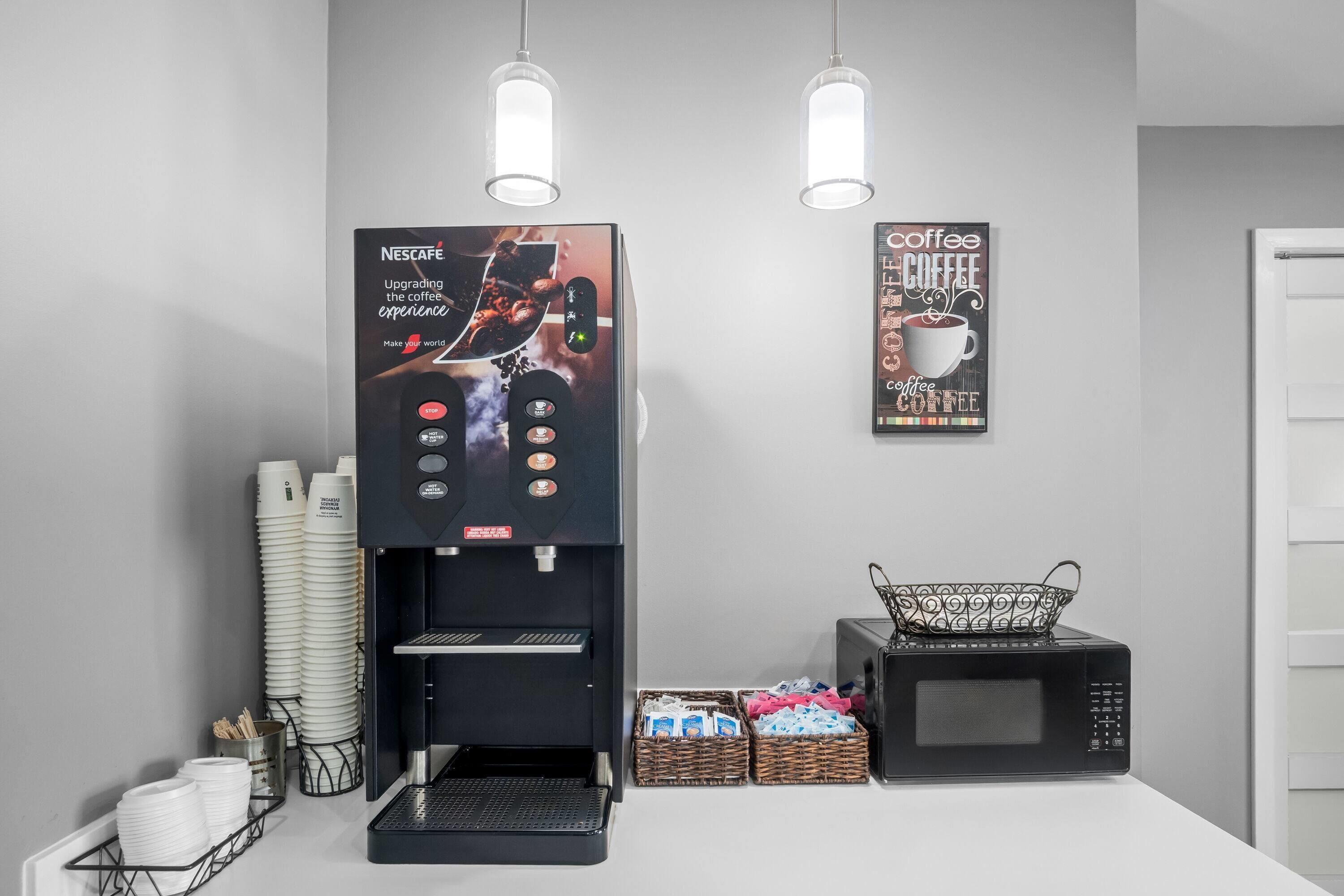 A coffee machine with a digital display and control panel, a microwave, and a coffee-themed poster on the wall.