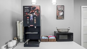 A coffee machine with a digital display and control panel, a microwave, and a coffee-themed poster on the wall. - Microtel Inn by Wyndham Georgetown (Georgetown)