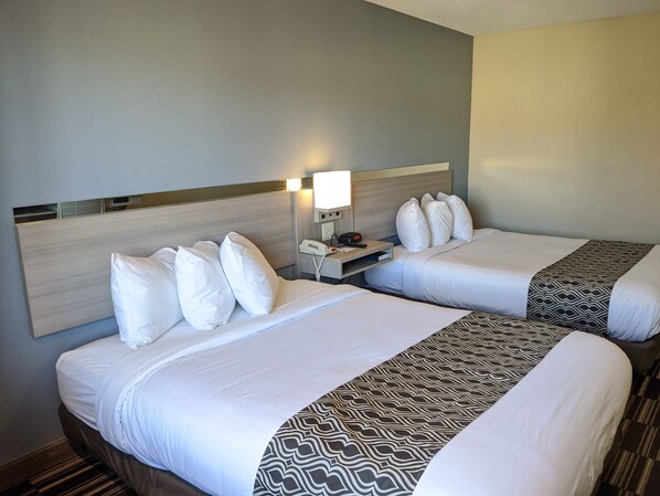 A hotel room with two beds, each with white bedding and a patterned throw. There is a bedside table with a lamp and a phone. - Microtel Inn by Wyndham Georgetown (Georgetown)