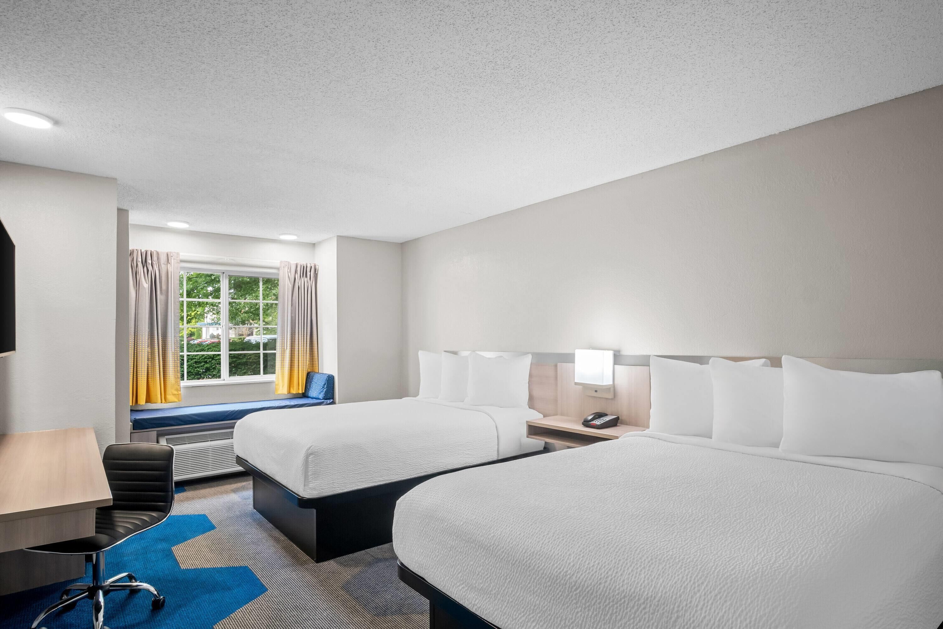 A hotel room with two beds, a desk, a chair, and a window with curtains.