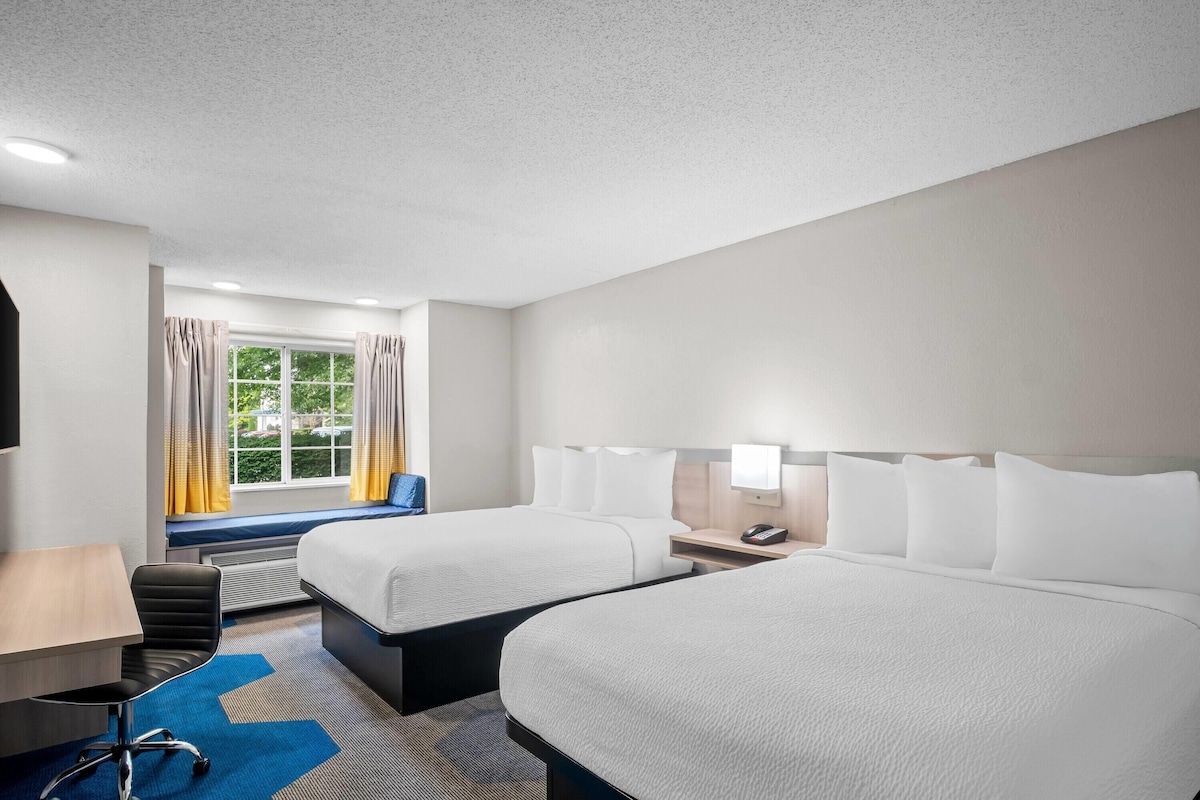 A hotel room with two beds, a desk, a chair, and a window with curtains.