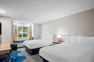 Habitación de hotel con dos camas, un escritorio, una silla y una ventana con cortinas.