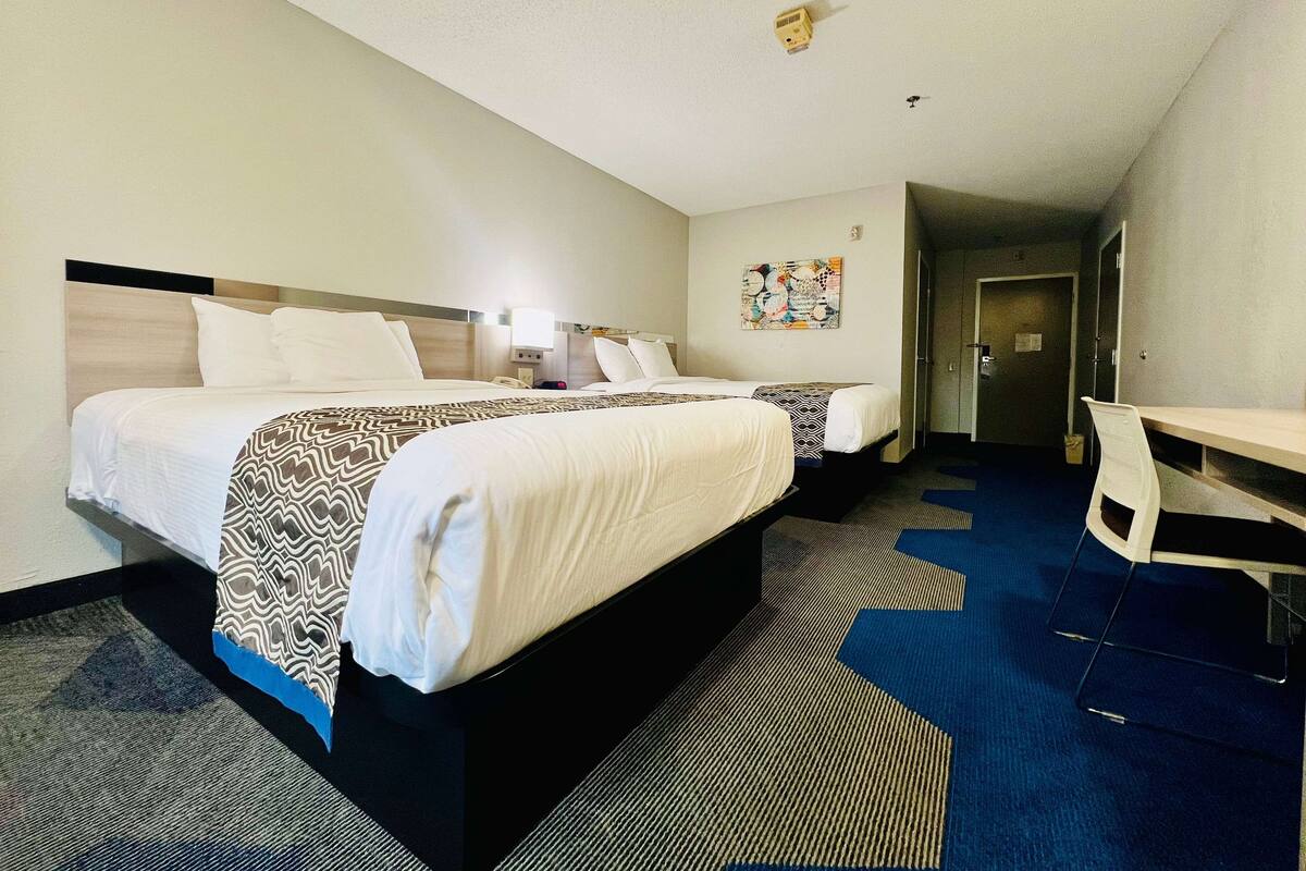 A hotel room with two beds, a desk, and a door leading to another room.
