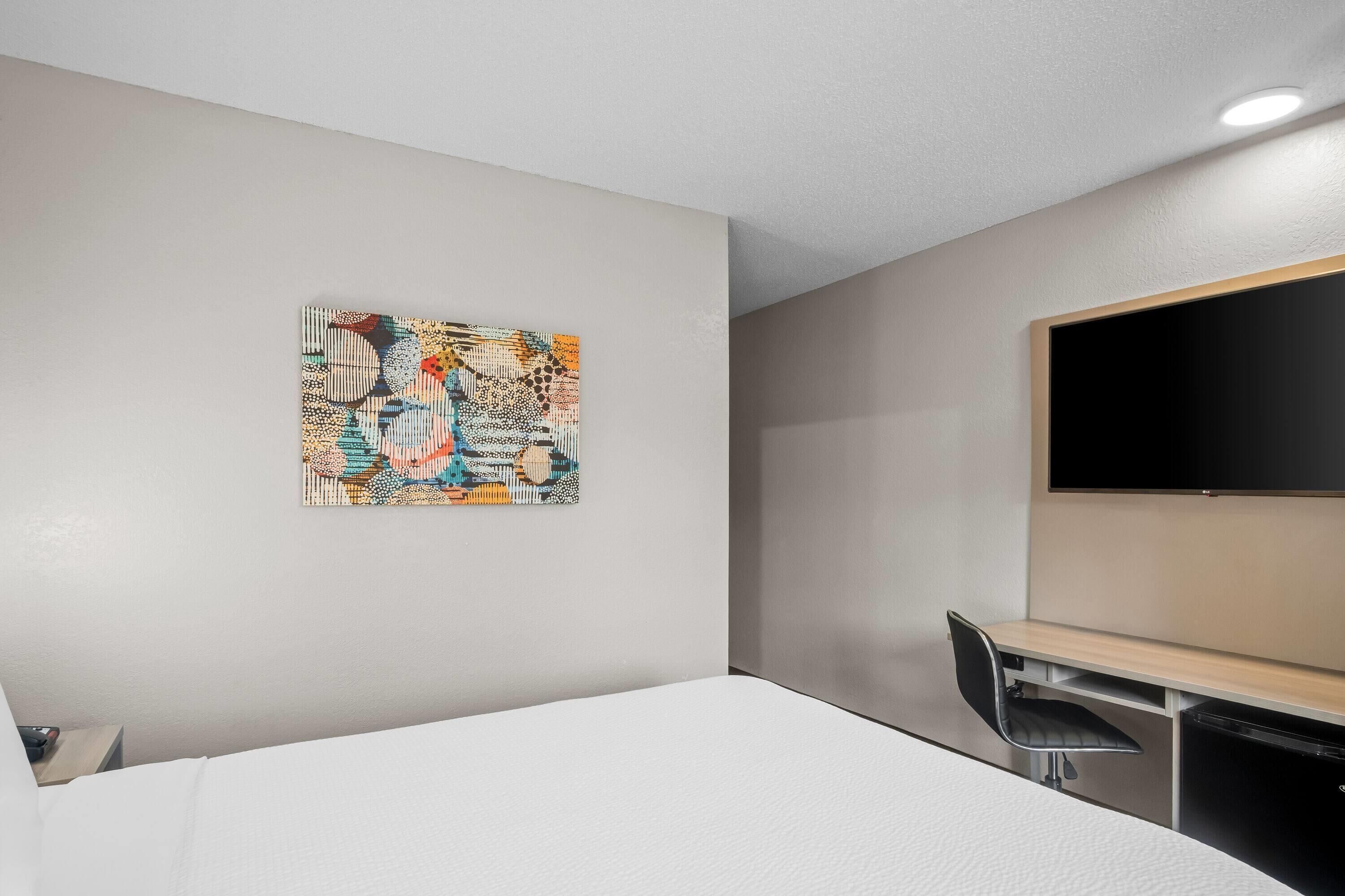 A hotel room with a bed, a desk, a chair, a flat-screen TV, and a wall-mounted artwork.