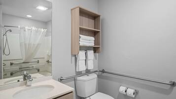 A bathroom with a sink, toilet, and a mirror. There is a wooden shelf above the toilet holding towels.
