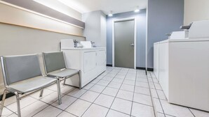 A clean, modern waiting area with two metal chairs, a washing machine, and a door in the background. - Microtel Inn by Wyndham Georgetown (Georgetown)
