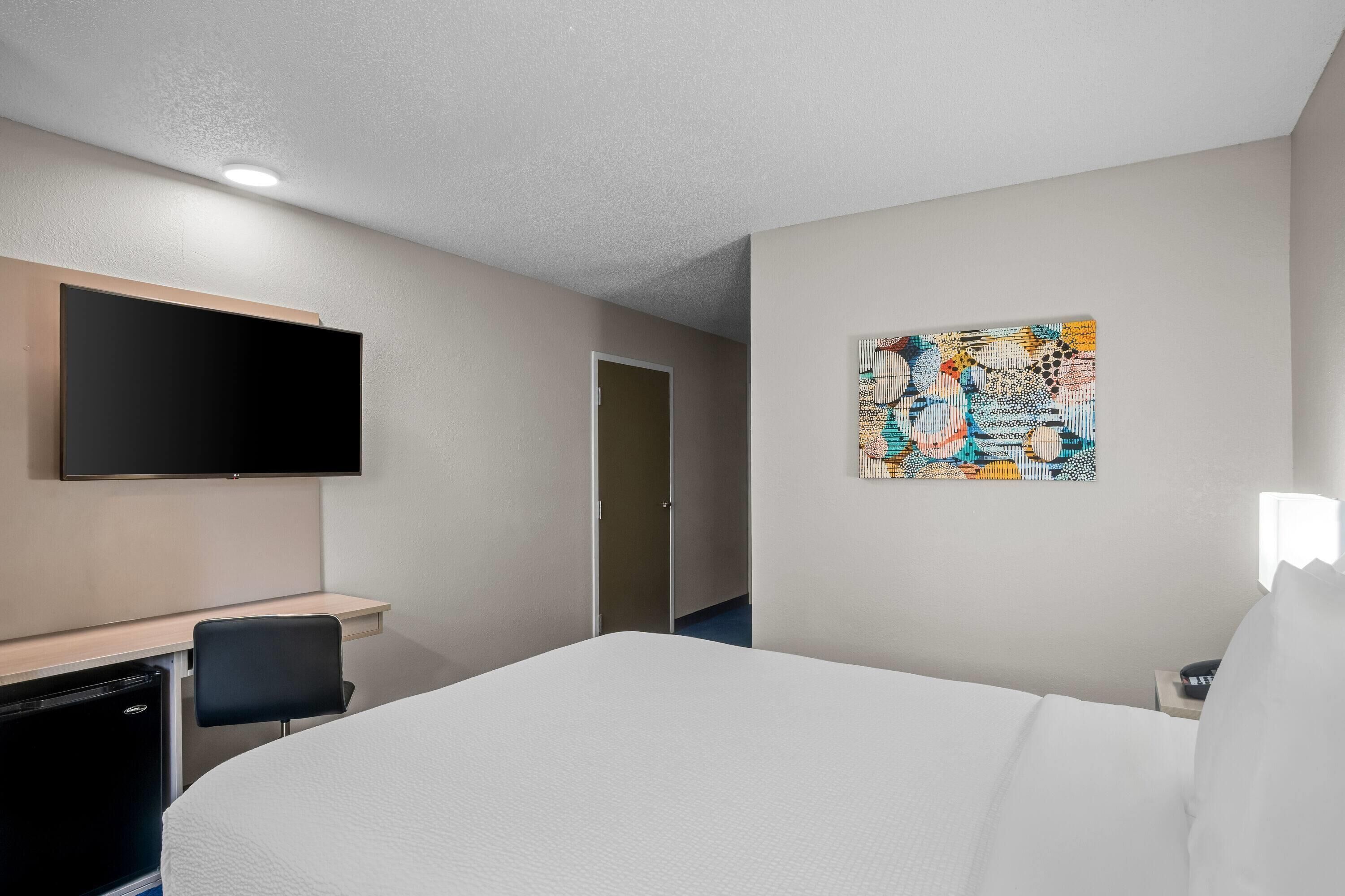 A hotel room with a bed, a desk, a chair, a television, and a door.