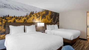 A hotel room with two beds, a large wall mural of a forest, a nightstand with a lamp, and a wooden floor.