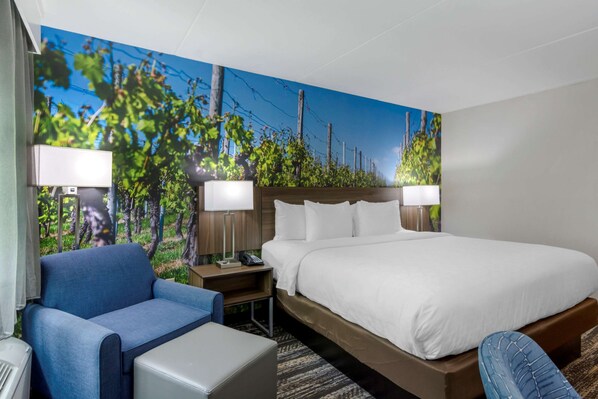A hotel room with a large bed, a blue armchair, a small table, and a nightstand with lamps.