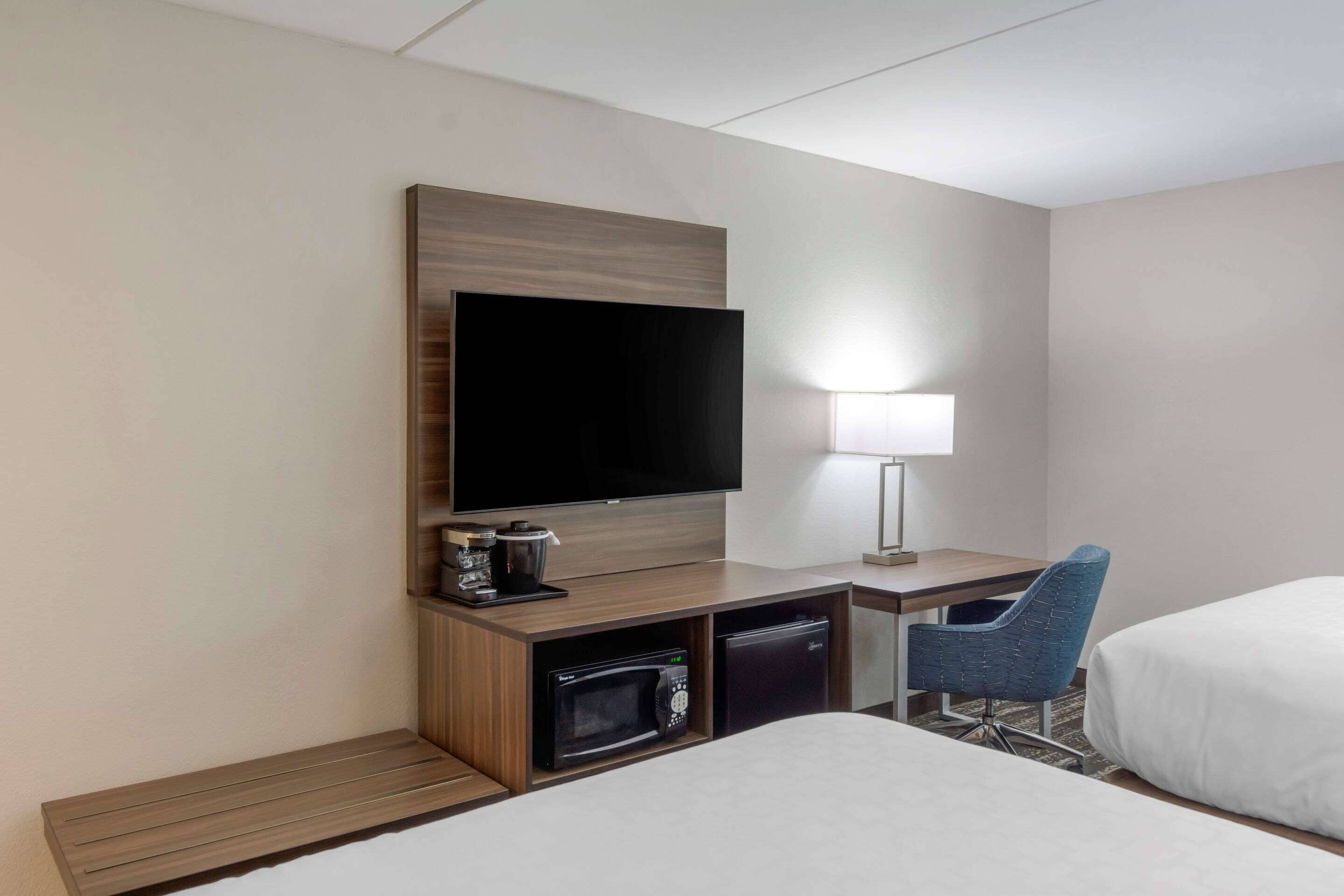 A hotel room with a TV, a desk with a lamp, a microwave, a coffee maker, and two beds.