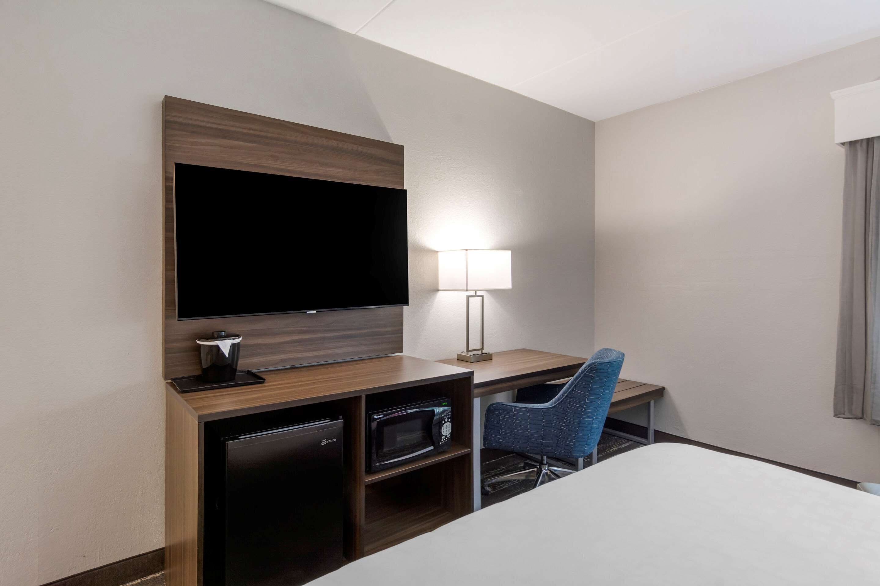 A hotel room with a flat-screen TV, a desk with a lamp, a microwave, and a blue chair.