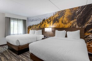 A hotel room with two beds, a large mural of a forest, a desk with a lamp, and a telephone.