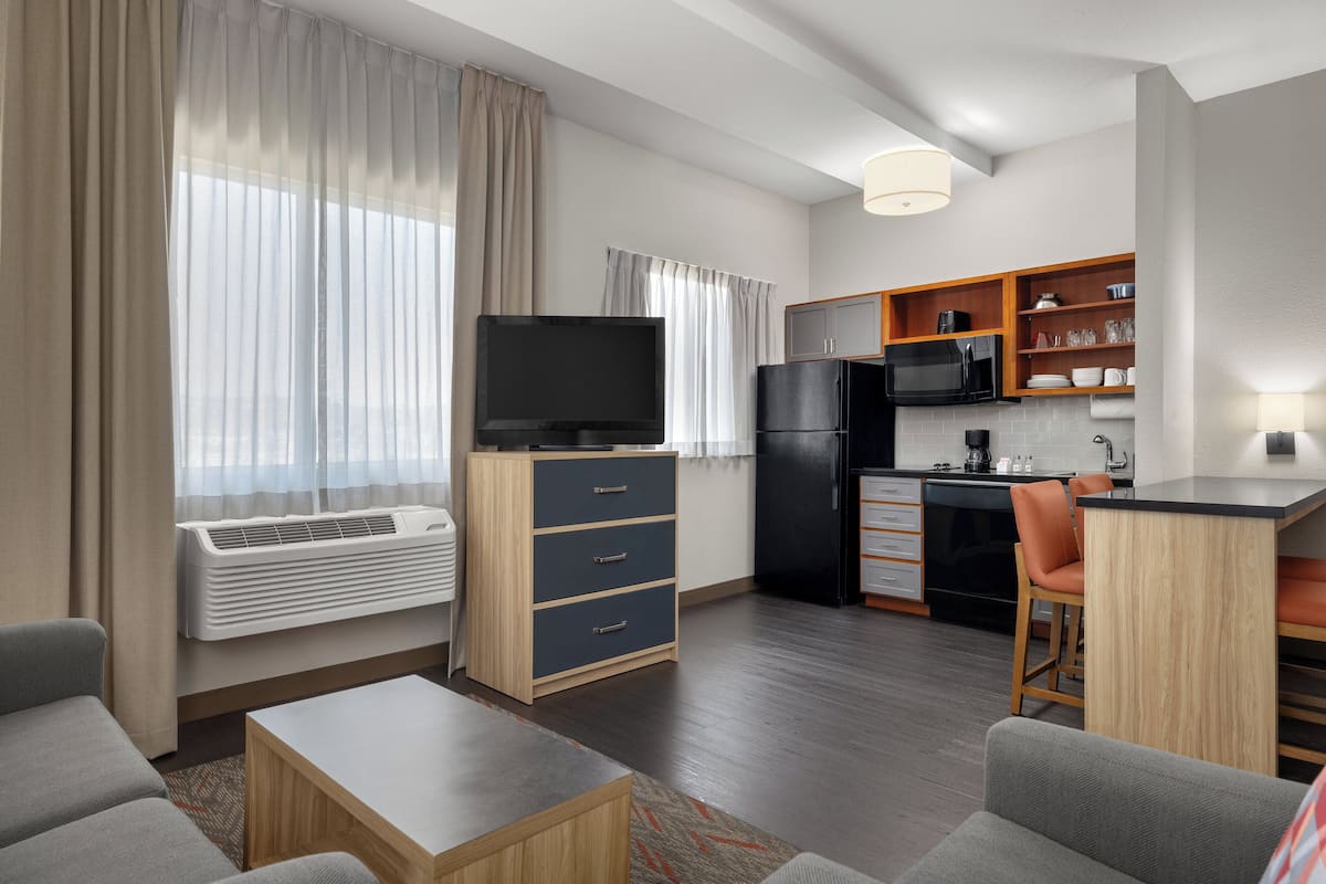 Een compacte hotelkamer met kitchenette, flatscreen televisie, bank en eethoek.