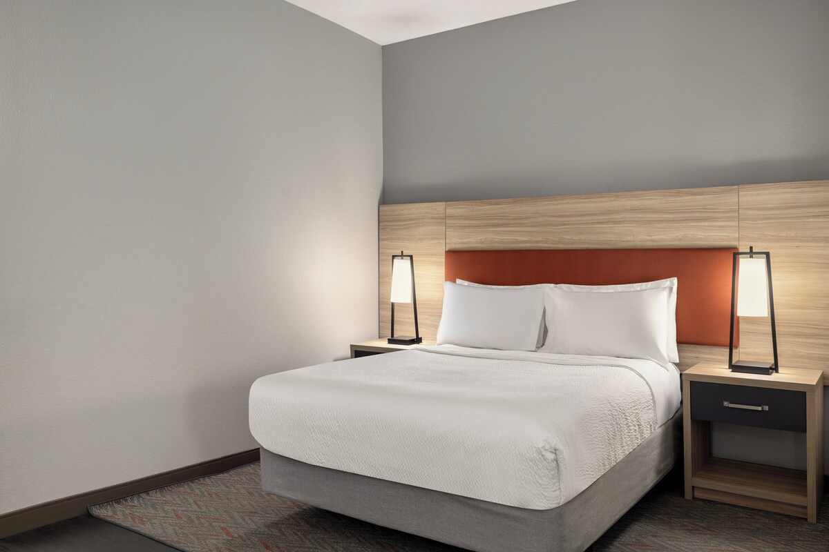 Una habitación de hotel con una cama, mesitas de noche y lámparas.