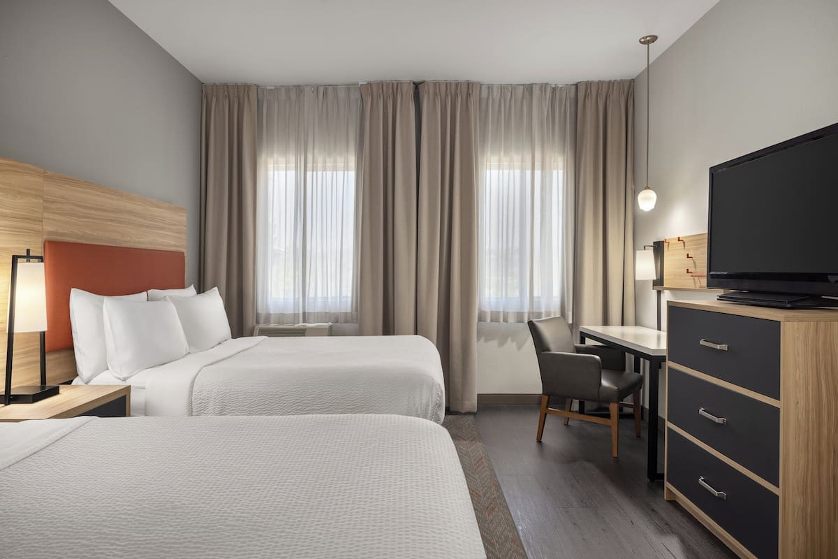 Een hotelkamer met twee bedden, een bureau, een stoel, een televisie en een kledingkast.