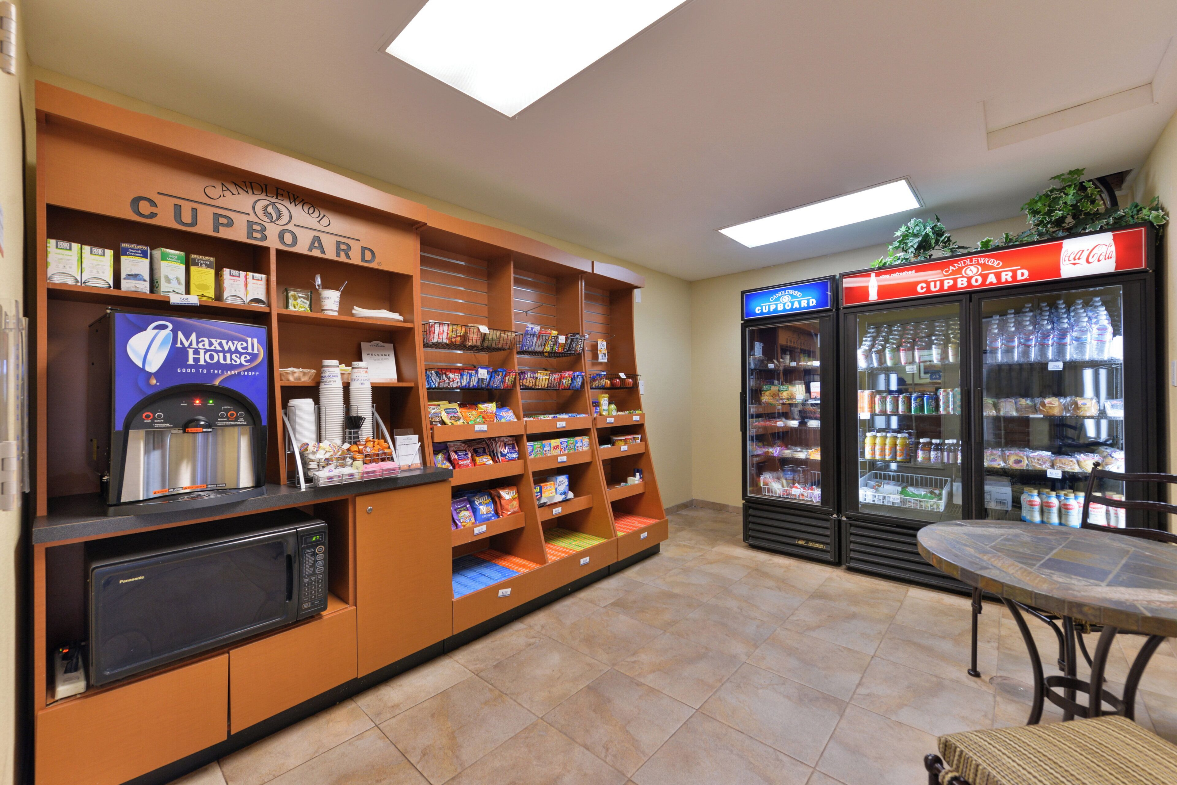 Un área de kitchenette con microondas, cafetera y refrigerador lleno de bebidas.