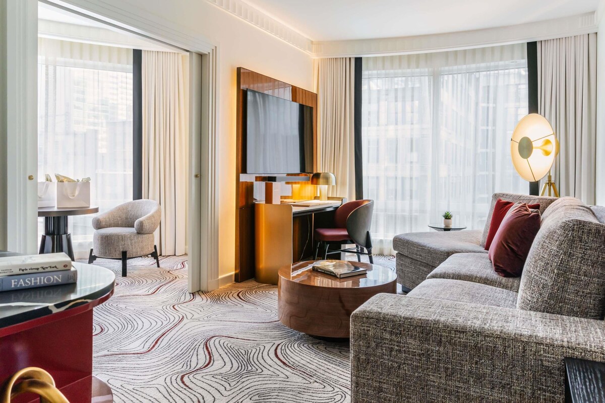 A modern hotel room with a sofa, armchair, and a small table with a lamp.