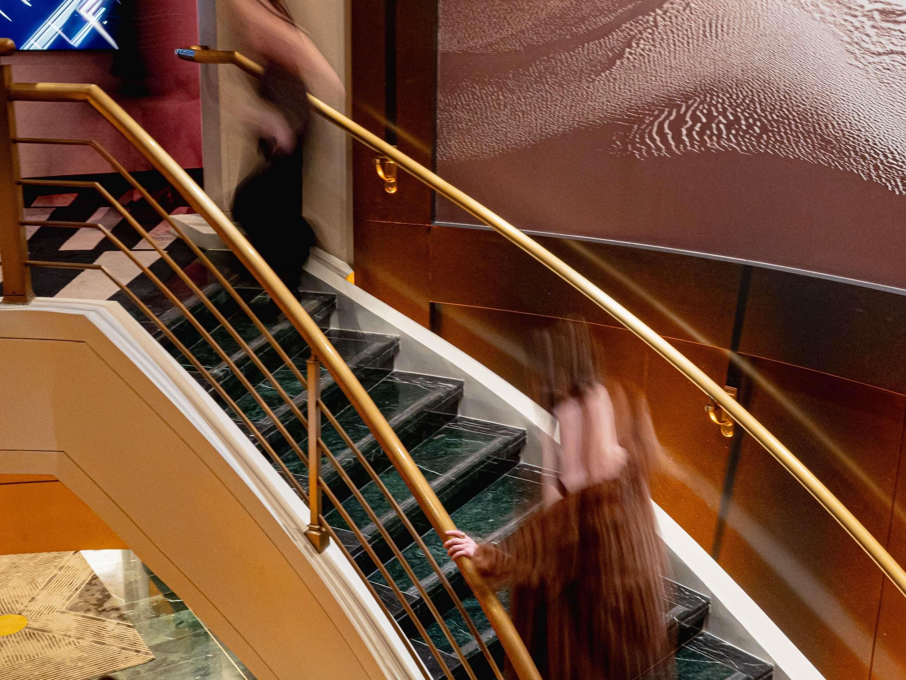 A staircase with a handrail, marble steps, and a patterned wall.