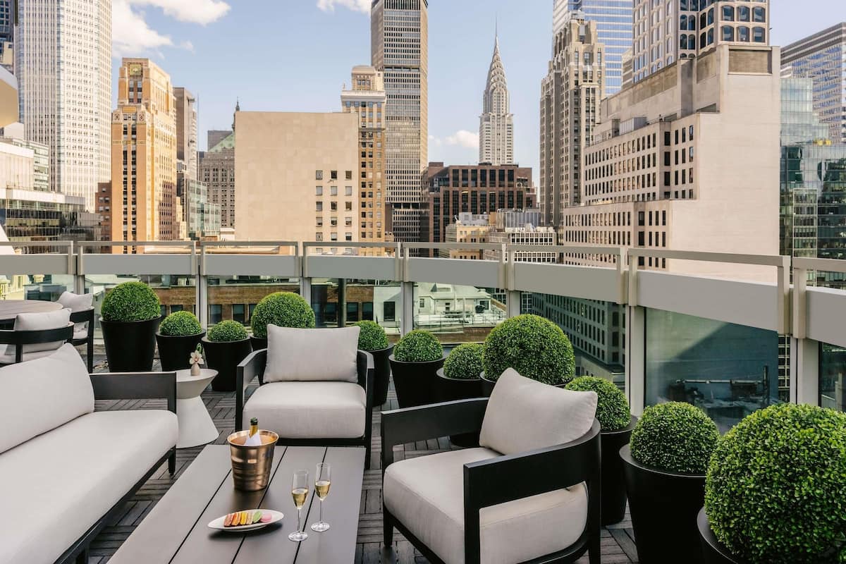 A rooftop terrace with outdoor seating, a champagne bucket, and a city skyline view.