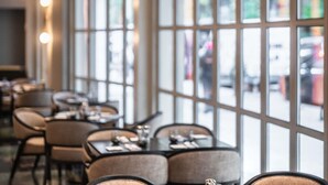 A restaurant interior with large windows, tables, and chairs arranged for dining.