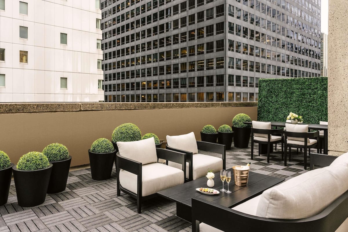 A rooftop terrace with outdoor seating, potted plants, and a view of a high-rise building.