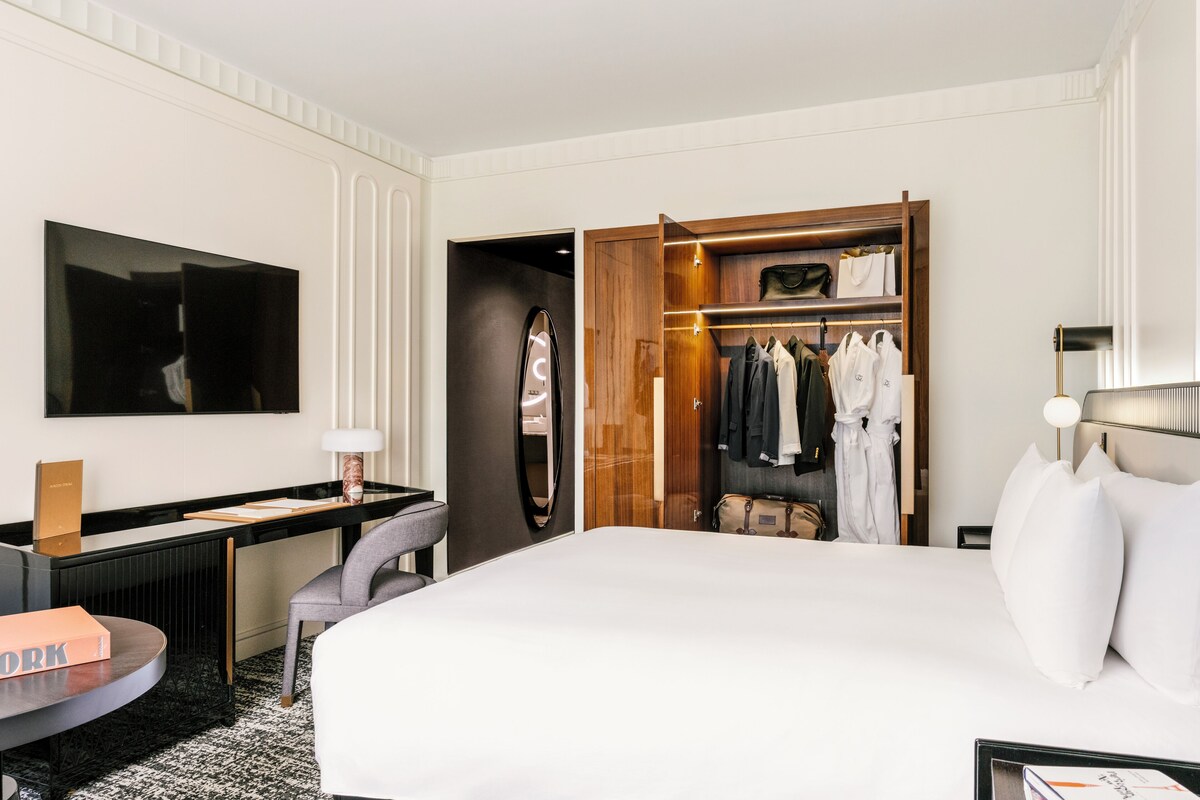 Una habitación de hotel moderna con una cama grande, un escritorio, una silla, un armario y un espejo.