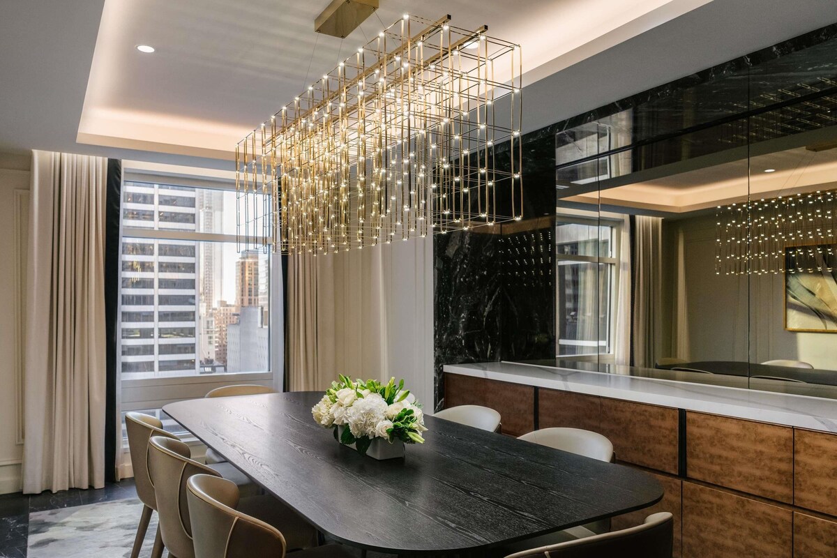A modern dining area with a dark wooden table, beige chairs, and a decorative light fixture.