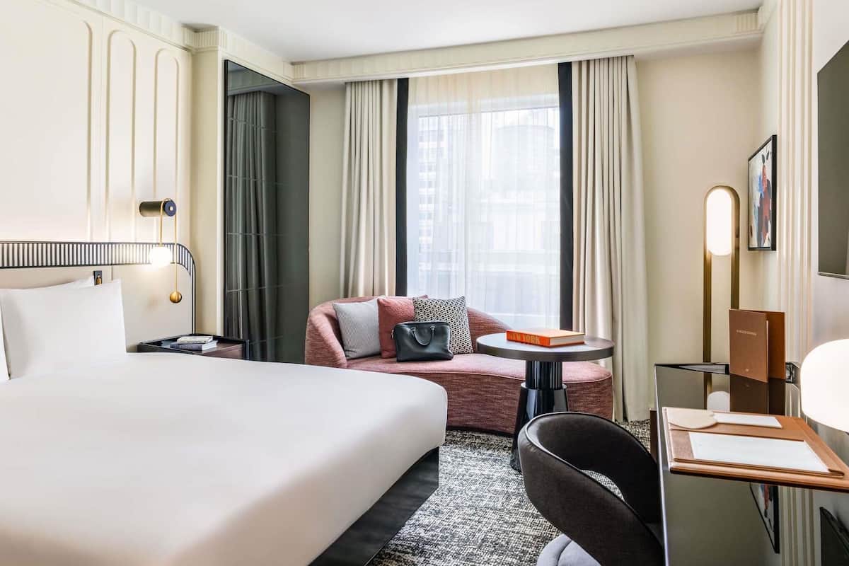 A hotel room with a bed, a desk, a chair, a sofa, and a window with curtains.