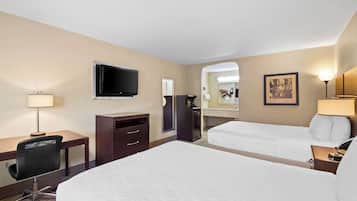 A hotel room with a large bed, a desk with a chair, a television, a desk lamp, a nightstand, and a bedside table.