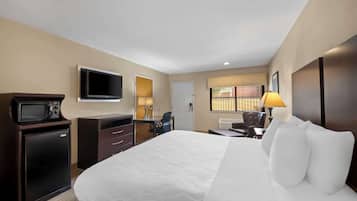 A hotel room with a bed, a desk, a chair, a TV, a microwave, and a small refrigerator.